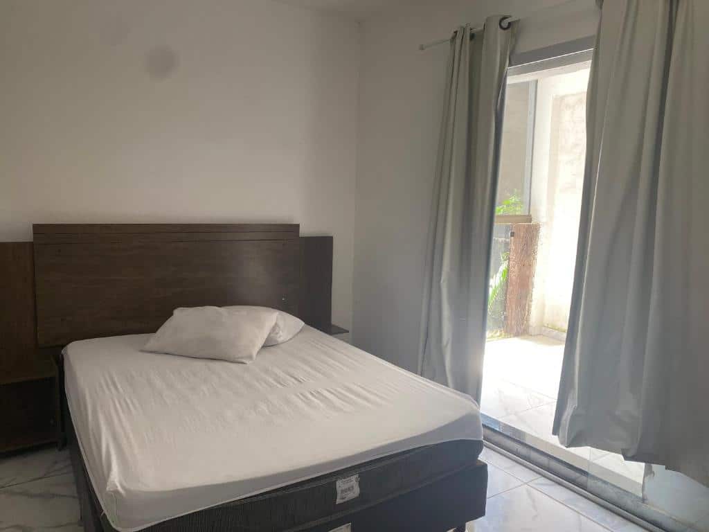 Foto do quarto do Apartamento para temporada Hospedagem. Ilustra o post sobre airbnb em Ouro Preto. Há uma cama box de casal à esquerda, e na direita dela, uma porta de vidro para o quintal.