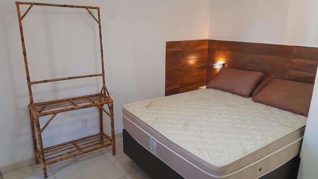 Quarto do airbnb Arraial do Cabo - Praia do Pontal. No lado esquerdo da imagem há uma arara para roupas feita de bambu e no lado direito há uma cama de casal com uma luminária no canto esquerdo da cama. Imagem utilizada para ilustrar o post airbnb em Arraial do Cabo.