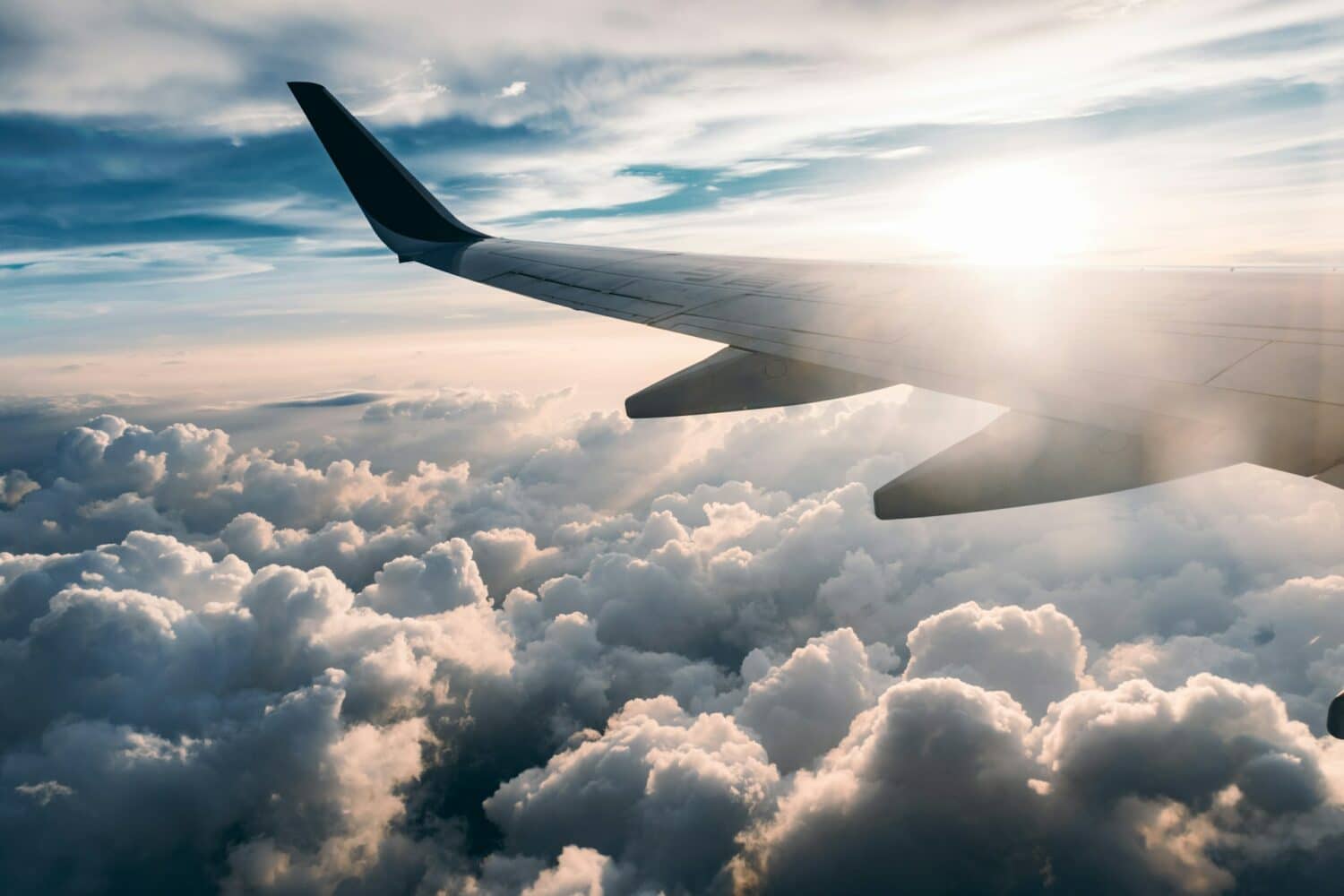 vista da asa do avião contra o por do sol e acima das nuvens brancas e fofinhas, para ilustrar o post de Seguro Viagem LATAM