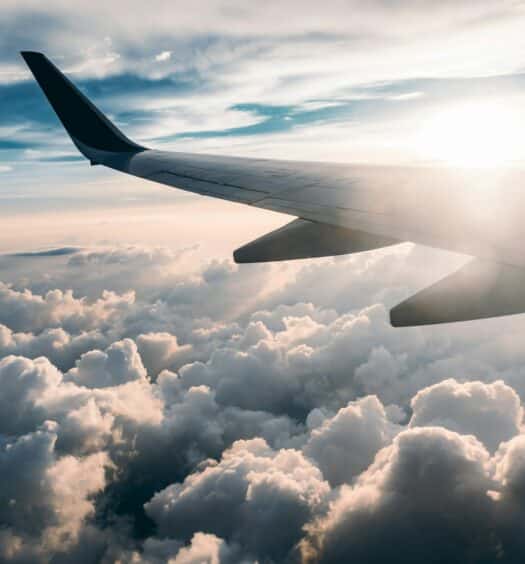 vista da asa do avião contra o por do sol e acima das nuvens brancas e fofinhas, para ilustrar o post de Seguro Viagem LATAM