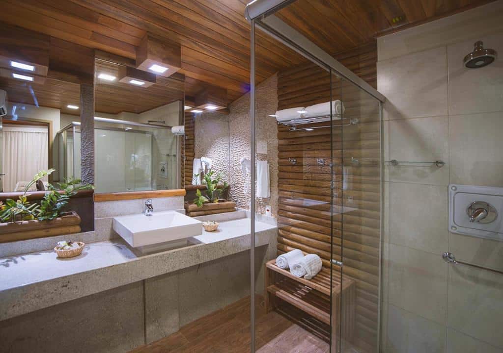 Banheiro da suíte dos Marechais com um box de vidro, uma parede com ripas de madeira e uma bancada com pia sobreposta e espelho fora a fora