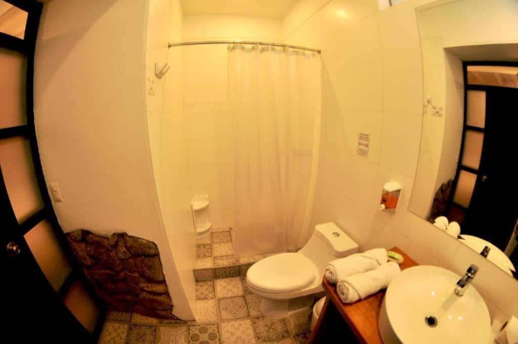 banheiro do Nao Victoria Hostel com uma cortina branca na ducha do chuveiro, uma vaso sanitário e uma pia com armário.