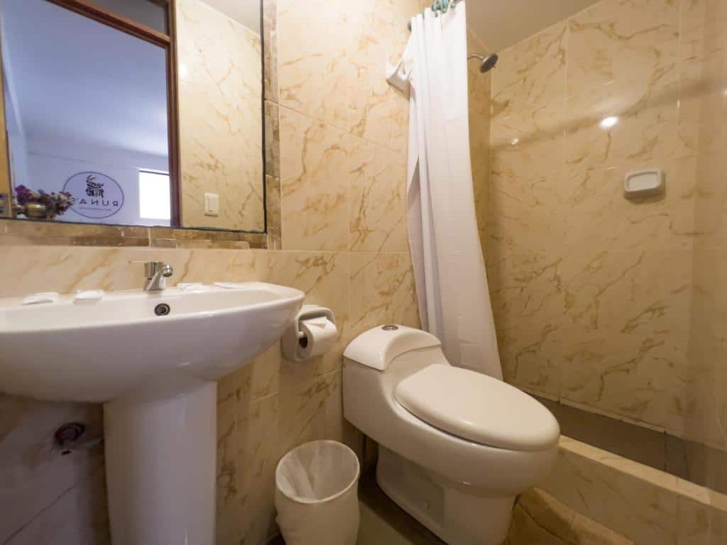 banheiro do Runas inn machupicchu com uma ducha no lado direito, um vaso sanitario e uma pia simples, ambos de louça brancas, e um espelho em cima da pia, no lado esquerdo.