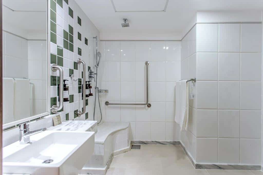 Banheiro com acessibilidade do Sauipe Grand Premium Brisa – All Inclusive com pia doa lado esquerdo da imagem a frente ao fundo chuveiro com barra de apoio.