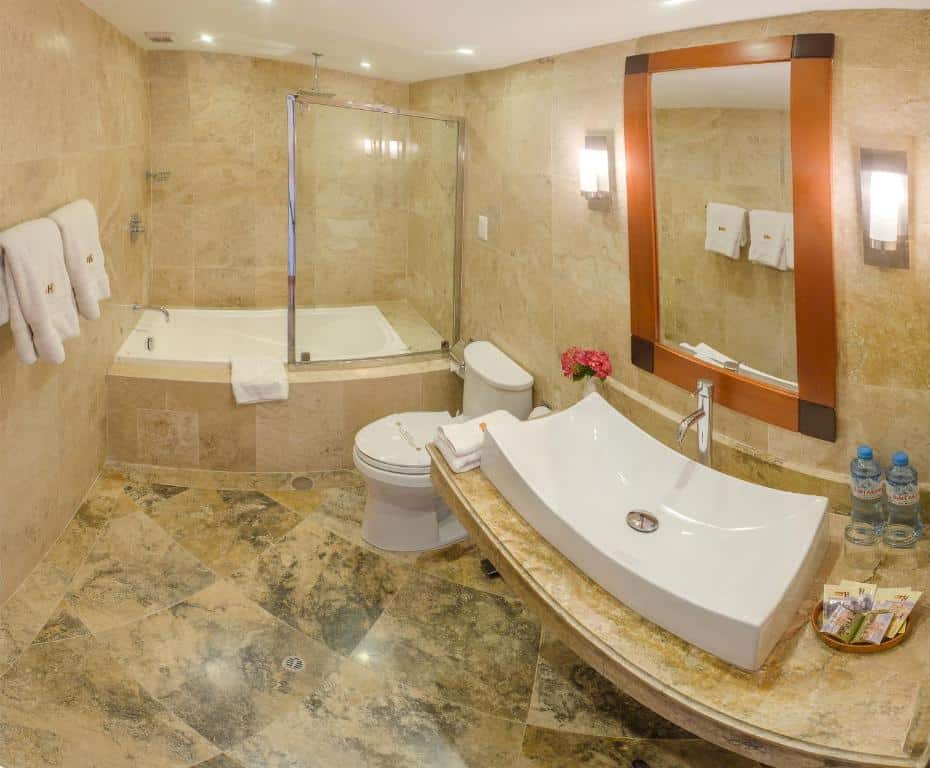 banheiro do Taypikala Hotel Cusco com uma banheira de hidromassagem, um vaso sanitário e uma pia. Todo o espaço é revestido em piso de pedra.
