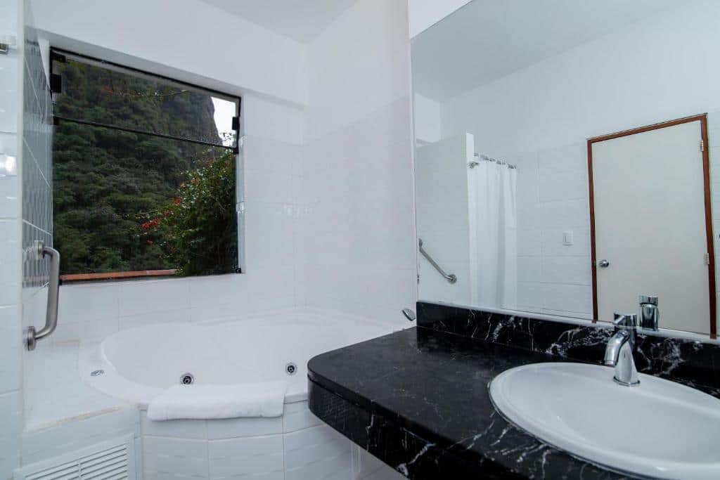 banheiro do tierra viva machu picchu hotel com uma banheira de hidromassagem no lado esquerdo e uma pia de pedra no lado direito, embaixo de um grande espelho