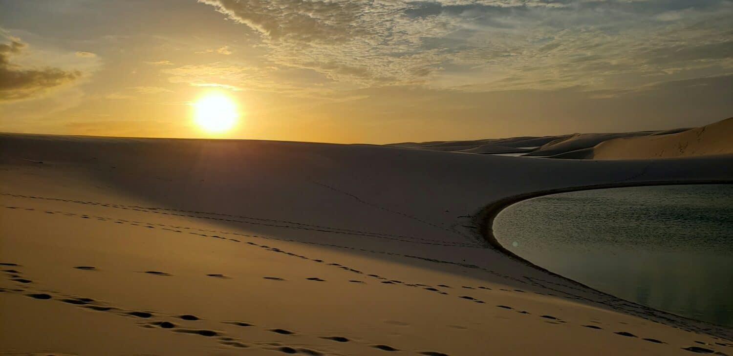 vista do pôr do sol Lençóis Maranhenses, em Barreirinhas, com dunas altas e um lago, o céu tem nuvens