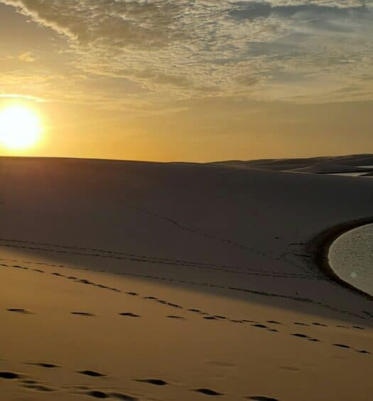 vista do pôr do sol Lençóis Maranhenses, em Barreirinhas, com dunas altas e um lago, o céu tem nuvens