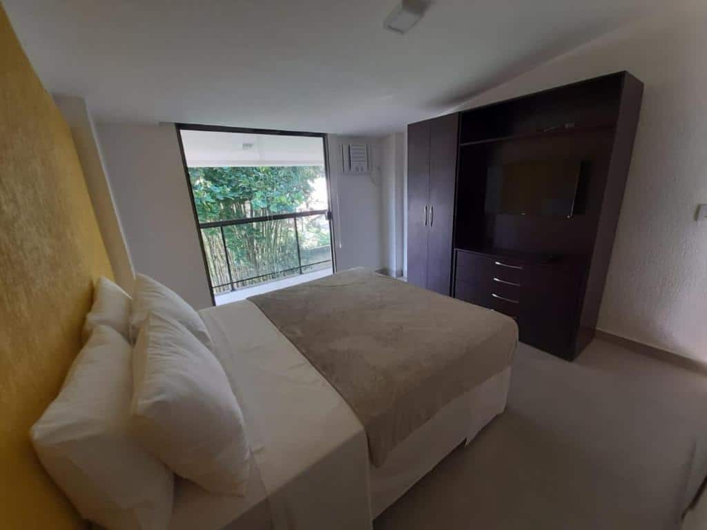Quarto do airbnb Bugio Flats. A cama de casal está encostada na parede do lado esquerdo do quarto, na frente da cama há um armário grande com uma TV no centro e no fundo há uma porta de vidro que dá acesso a varanda. Imagem para ilustrar o post airbnb em Ilha Grande.