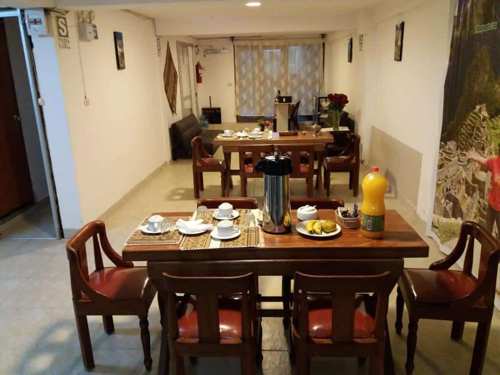 mesa de madeira para seis lugares no refeitório do hotel com vários itens de café da manhã dispostos em cima, como xícaras de café e pães e bolos.