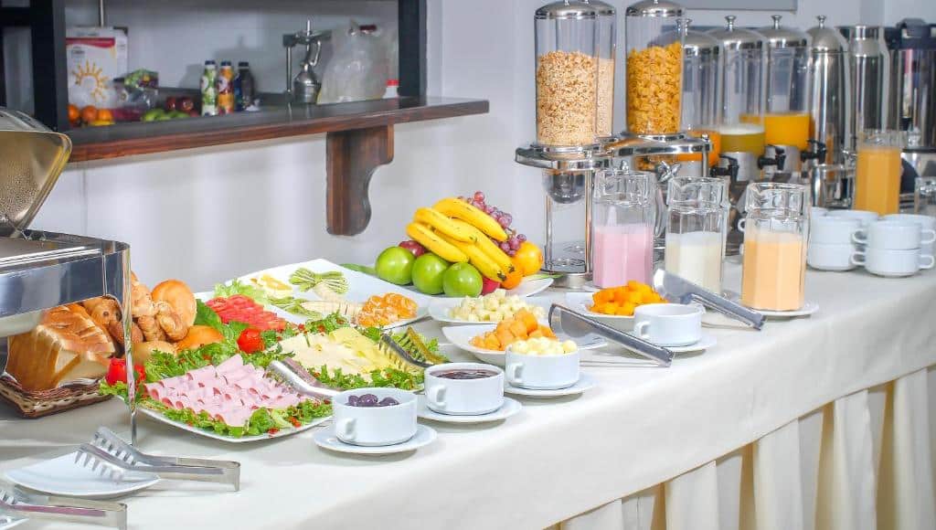 mesa de café da manhã do hotel golden sunrise com vários pratos de frutas e frios, como presunto e queijo, além de jarras de suco e iogurte