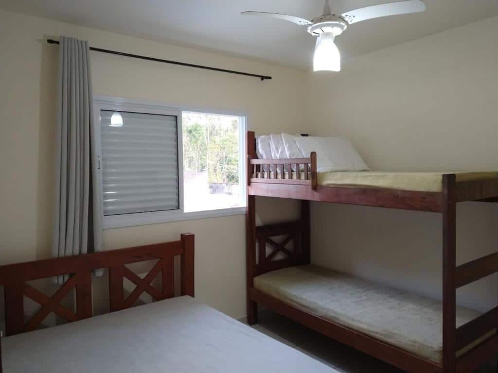 Quarto do Canto Verde Aptos I, um dos airbnb em Caraguatatuba. Uma beliche está encostada na parede ao lado direito, e uma janela a separa da cama de casal. Quatro travesseiros estão disponíveis na cama de cima da beliche.