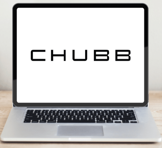 Um notebook aberto sob uma mesa de madeira, ele está na página inicial do site da seguradora Chubb, para representar seguro viagem Chubb