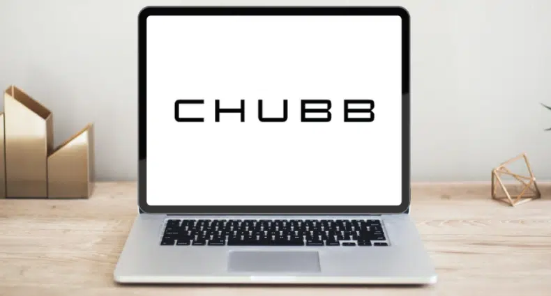 Um notebook aberto sob uma mesa de madeira, ele está na página inicial do site da seguradora Chubb, para representar seguro viagem Chubb