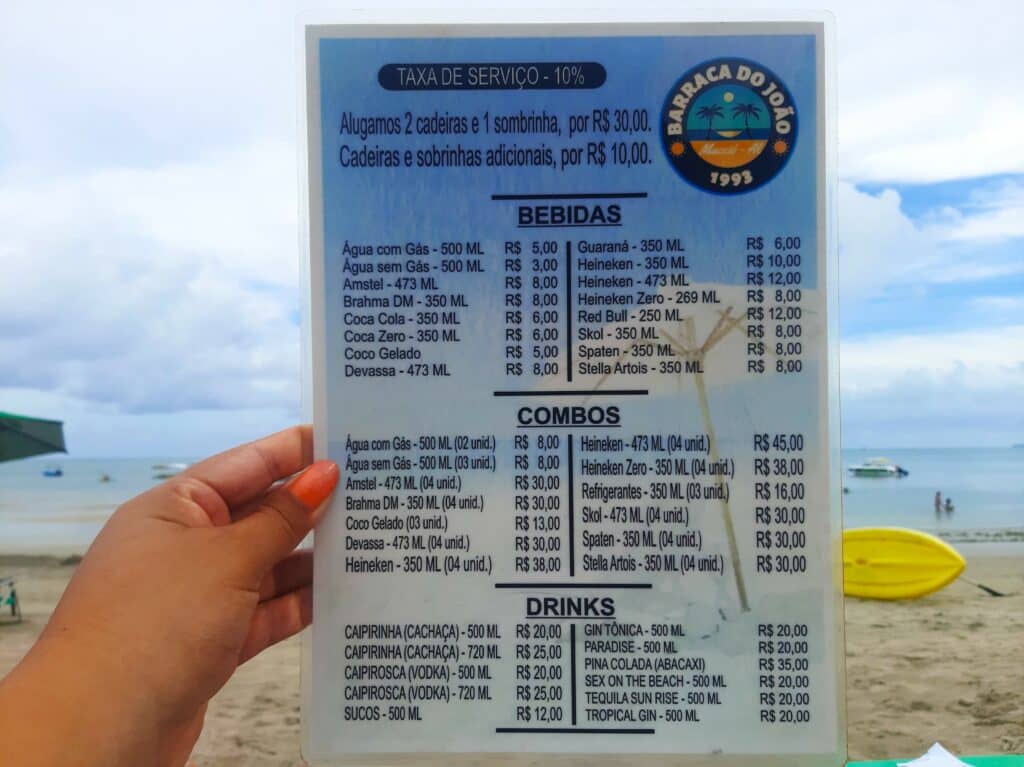 Mão de uma mulher segurando um cardápio na praia em Maceió