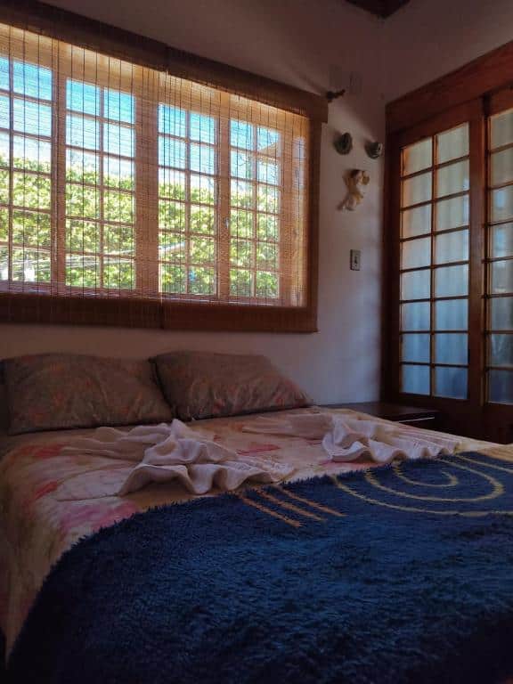Foto do quarto da Casa com vista verde. Ilustra o post sobre airbnb em Ouro Preto. Vemos a cama de casal de frente, e atrás dela há uma janela. 