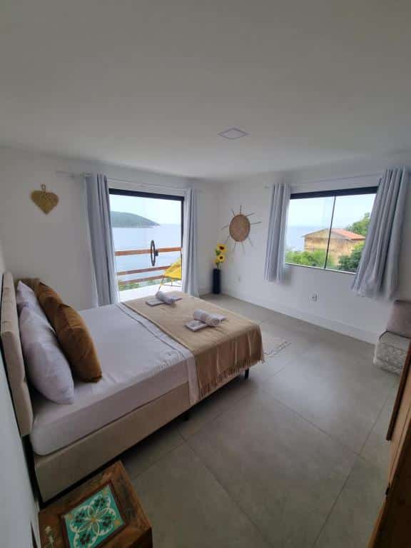 Quarto do airbnb Casa Corazul. A cama de casal está encostada na parede do lado esquerdo da imagem e na parede em frente a cama há uma janela de vidro. Na parede ao lado esquerdo da cama há uma porta de vidro que dá acesso a varanda. Imagem utilizada para ilustrar o post airbnb em Arraial do Cabo.