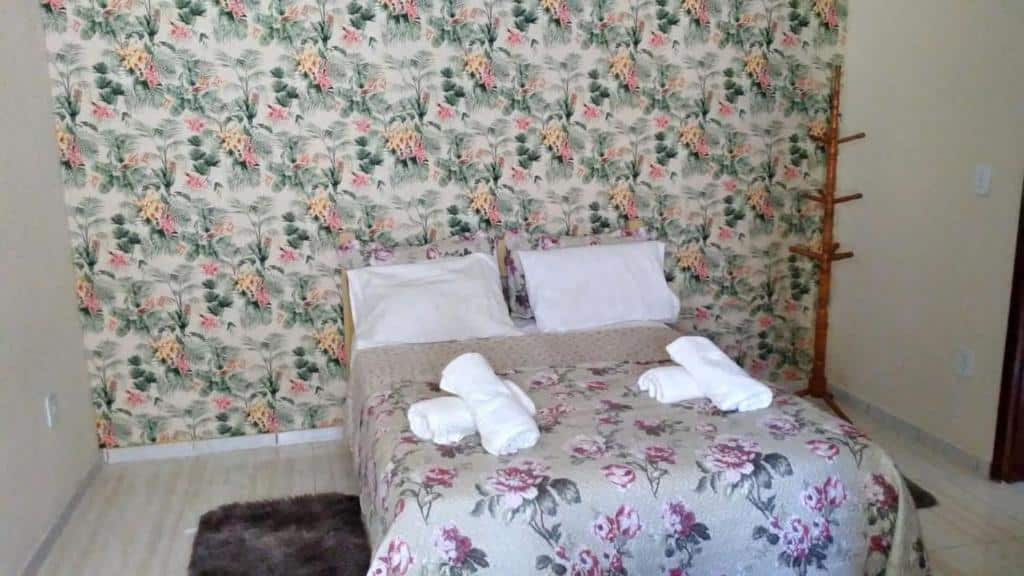 Quarto do airbnb Casa da Celia. No centro do quarto há uma cama de casal, no lado esquerdo da cama é possível ver parte de um tapete no chão e no lado direito da cama há um cabideiro. Imagem utilizada para ilustrar o post airbnb em Arraial do Cabo.