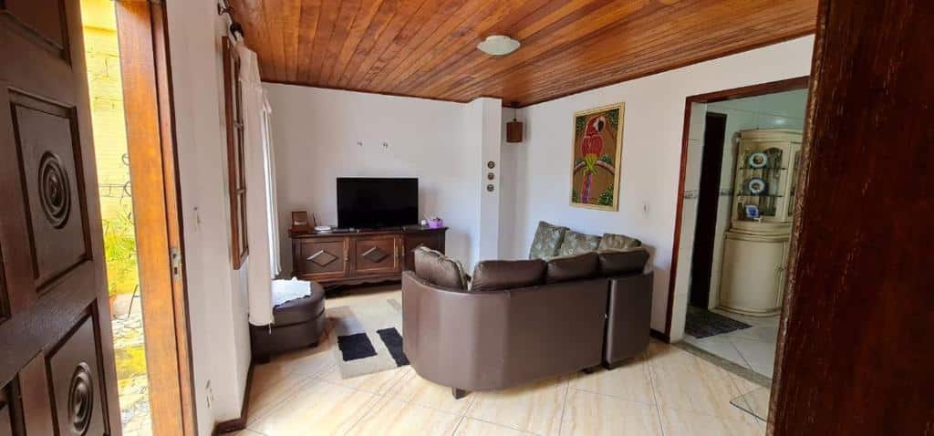 Sala espaçosa na Casa Ouro Preto No meio há um sofá, e na frente dele uma rack com TV em cima. Na esquerda há uma porta, e na direita, uma passagem para a cozinha.
