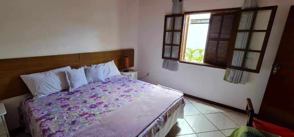 Foto do quarto da Casa Ouro Preto. Ilustra o post sobre airbnb em Ouro Preto. Na esquerda há uma cama de casal, e ao lado direito dela, uma janela de madeira. 