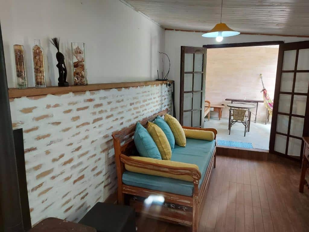 Sala na Casa Paúba 80m do Mar. Vemos a lateral do ambiente. Há um sofá à esquerda e uma porta para a varanda no fundo, ao lado do sofá, onde há uma mesa, sofá e rede de descanso.