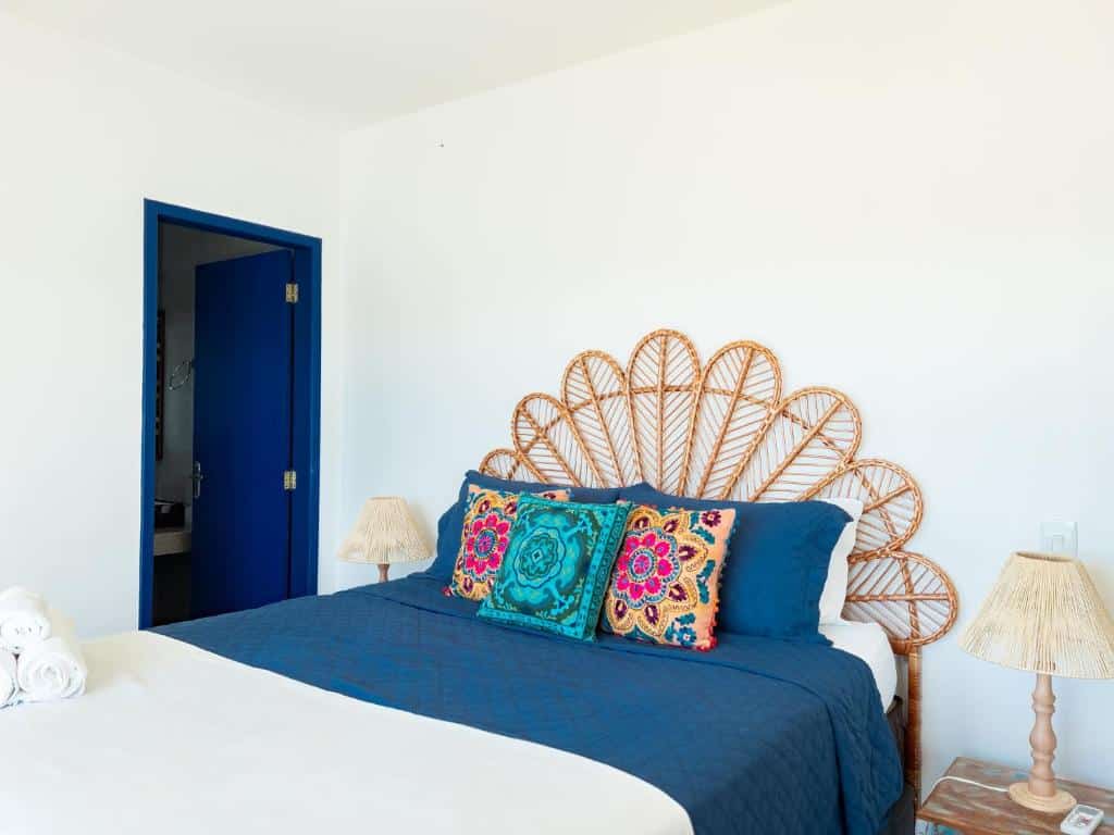 Quarto do airbnb Casa Santorini Terrace. No canto esquerdo da imagem há uma porta que dá acesso ao banheiro, no meio do quarto está a cama de casal e em cada lado da cama há uma mesa de cabeceira com um abajur em cima. Imagem utilizada para ilustrar o post airbnb em Arraial do Cabo.