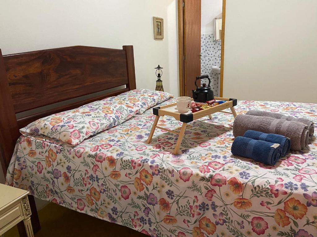 Foto do quarto do Chácara das Araucárias. Representa o post sobre airbnb em São Francisco Xavier. A cama é de casal e em cima dela há toalhas e uma bandeja de madeira com café da manhã. Ao lado da cama há uma porta para o banheiro.