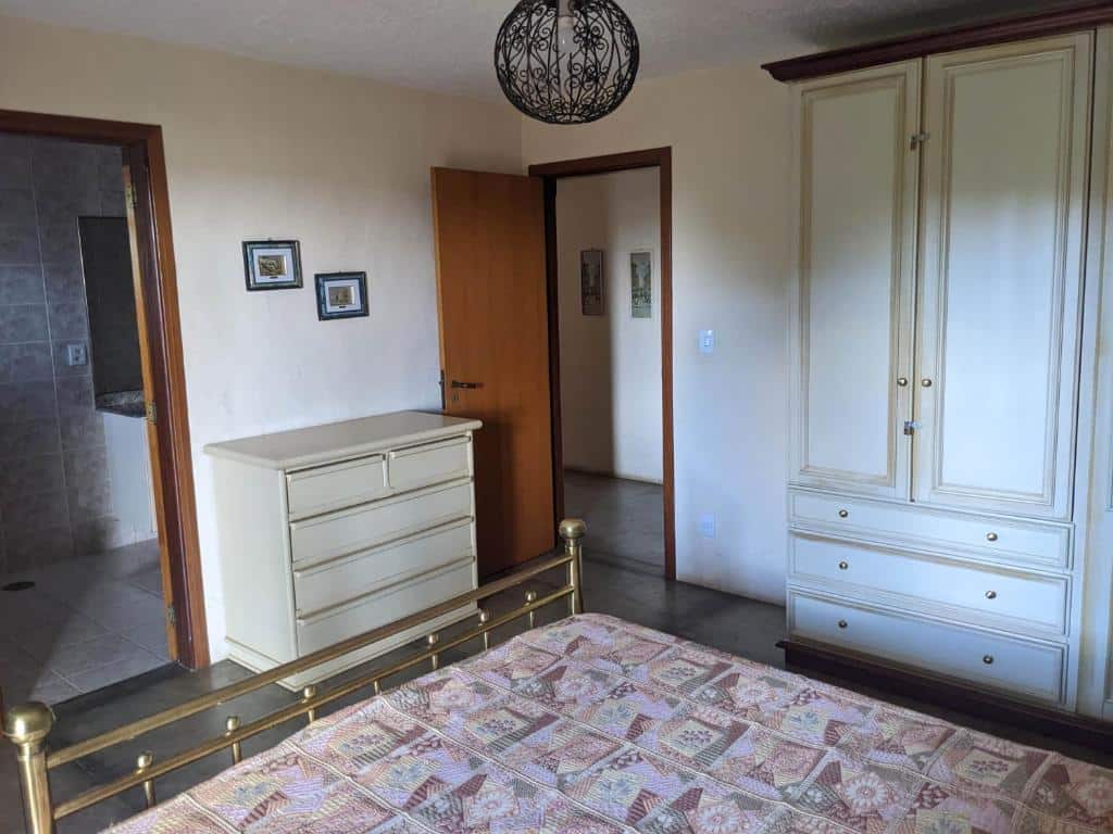 Foto do quarto em Chácara Santa Terezinha. A cama está no meio, vemos ela como quem está sentado. O guarda-roupa está ao lado direito, e também a porta do quarto. De frente há uma cômoda e porta para o banheiro, mais à esquerda.
Ilustra o post sobre airbnb em Serra Negra.