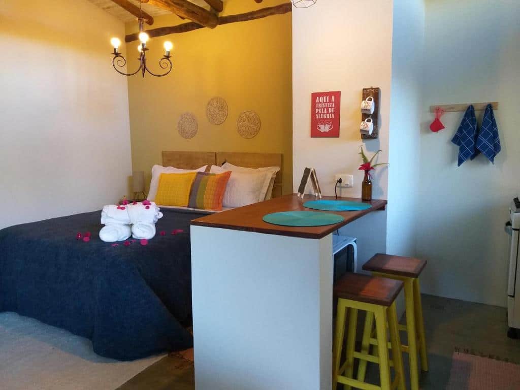 Foto do quarto do Chalé Alecrim. Representa o post sobre airbnb em São Francisco Xavier. A cama está à esquerda, ao lado dela há uma bancada da cozinha com dois bancos.