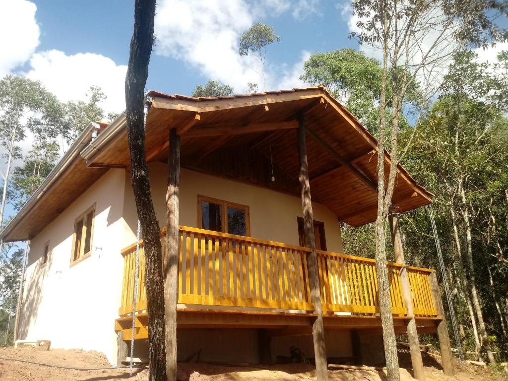 Parte externa do Chalé Morada das estrelas que mostra a construção do chalé com uma cor bege, janelas, porta, varanda e telhado de madeira. Em volta do chalé tem várias árvores, imagem ilustrando post Airbnb em Aiuruoca.