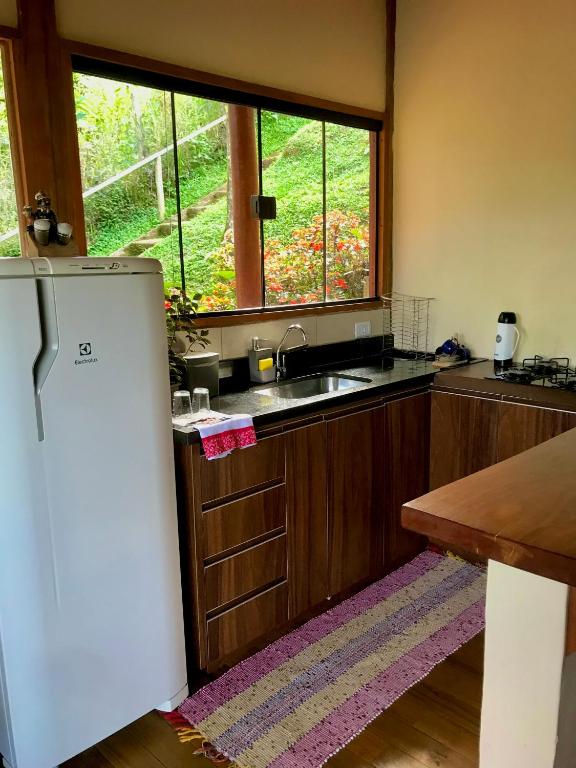 Foto de uma cozinha com geladeira, armários, pia, fogão e janela no Chalé nas Árvores.