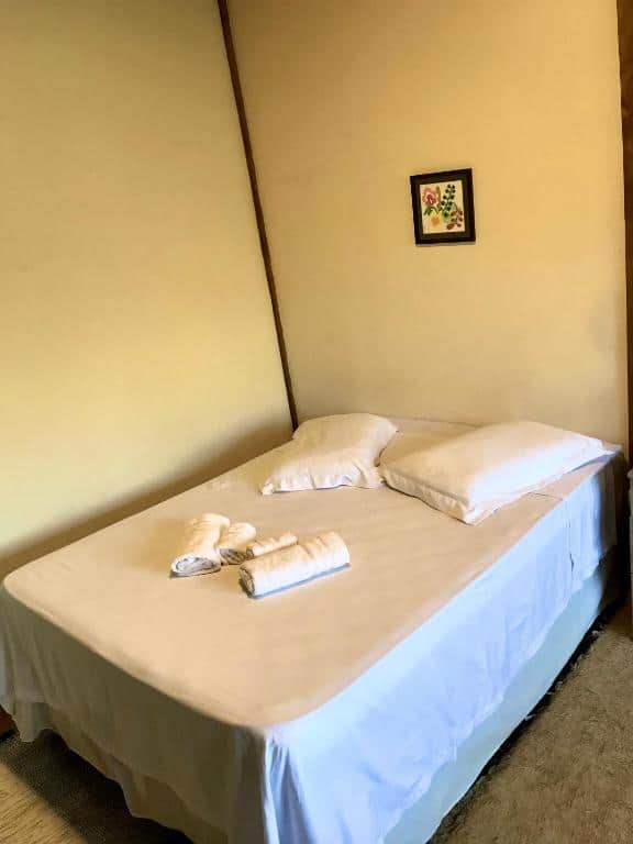 Foto do quarto do Chalé nas Árvores. Representa o post sobre airbnb em São Francisco Xavier. A cama é box de casal, possui toalhas em cima e as paredes são brancas.
