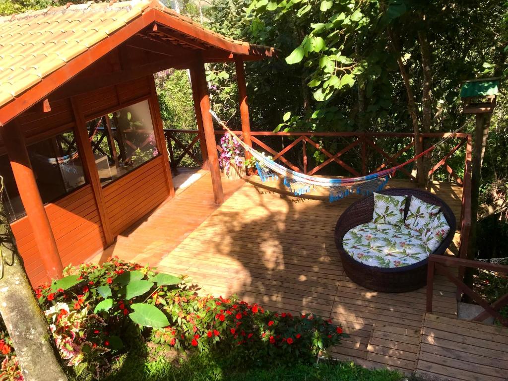 Varanda do Chalé nas Árvores. O chão é de madeira, no ambiente estão uma rede, poltrona com almofas e plantas ao redor.
