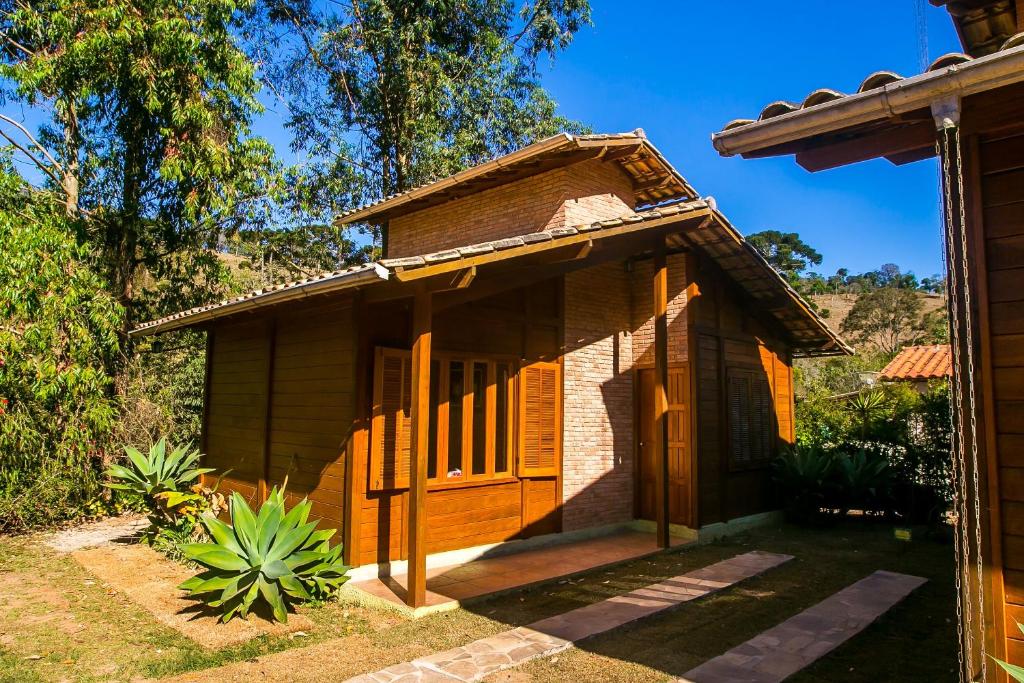 Parte externa do Chalés Belo Vale - Rua do Curro que mostra a construção de madeira e tijolos com duas janelas de madeira e uma porta de madeira. Em volta do chalé tem algumas plantas e árvores em volta e um gramado verde. Imagem ilustrando post Airbnb em Ibitipoca.
