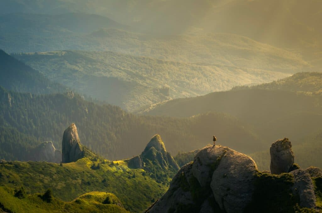 uma pessoa parada em cima de montanhas altas em um vale verdejante no Ciucaș Peak, na Romênia