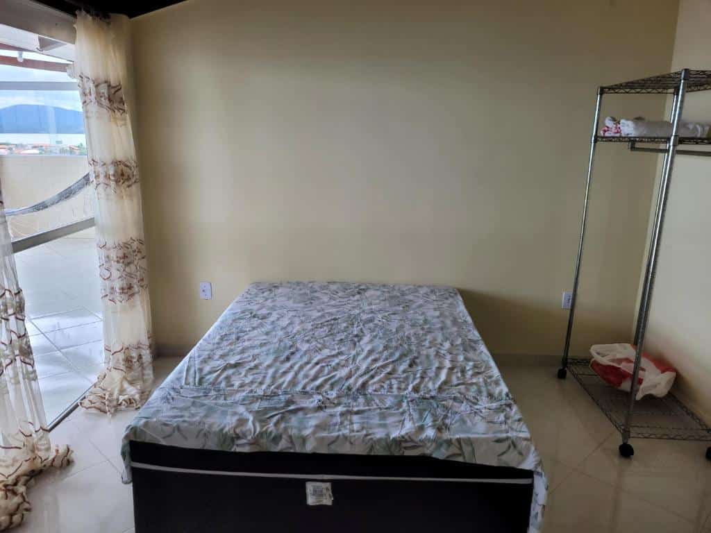 Quarto da Cobertura vista mar. Uma cama box de casal no meio, do lado direito uma estante, do lado esquerdo a varanda do quarto.