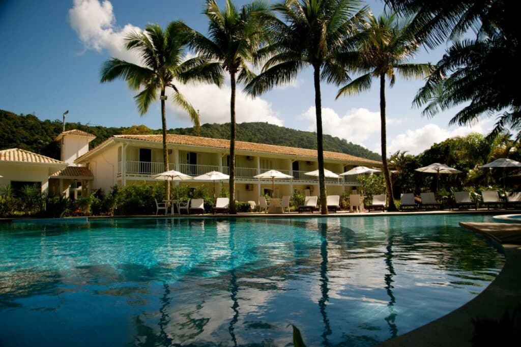 Piscina do Costa Verde Tabatinga Hotel cercada por espreguiçadeiras, guarda-sóis e palmeiras. Ao fundo é possível ver a longa extensão da propriedade. Representa airbnb na praia de Tabatinga