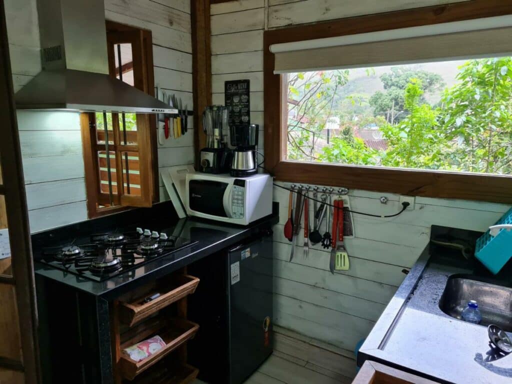 Cozinha do Chalé Paúba 80m do Mar com pia do lado direito da imagem e do lado esquerdo um balcão com fogão e micro-ondas em cima e abaixo uma geladeira. 
