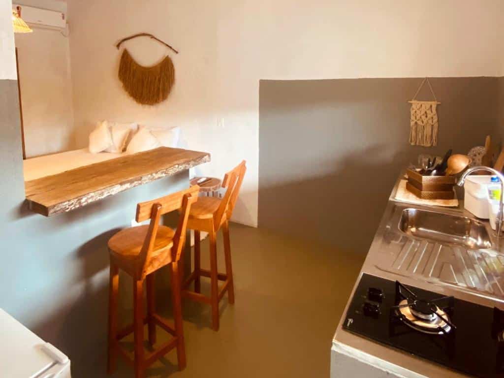 Cozinha do Lá na Chay Hospedaria Caraíva – Xandó com pia e fogão do lado direito da imagem e do lado esquerdo um balcão com duas cadeiras.