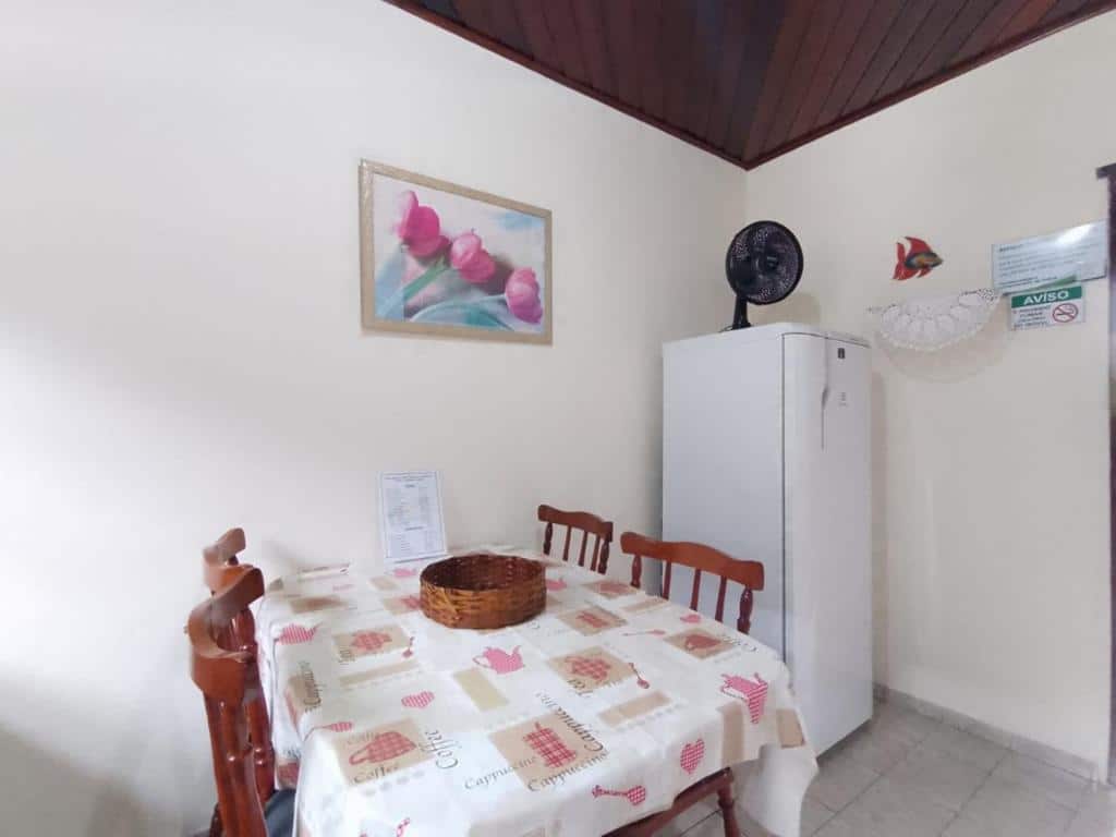 Cozinha do Praialar Apartamentos Ubatuba com mesa de madeira com quatro cadeiras do lado esquerdo da imagem do lado direito a geladeira.