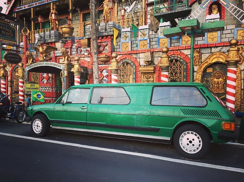 Uma foto tirada em frente a um prédio em Serra Negra, chamado Disneylândia dos Robôs. É colorido e divertido, uma atração para crianças. Uma limousine antiga verde está passando na frente do local.