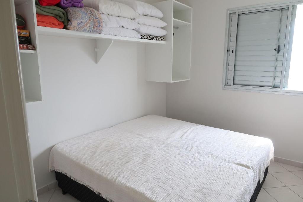 Quarto do Doce Lar de Bertioga frente ao Mar, um dos airbnb em Bertioga. Uma cama de casal está logo abaixo de um armário com travesseiros e jogos de cama. Na parede ao lado direito fica uma janela.