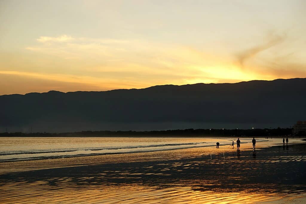 Pessoas caminhando perto do mar durante o pôr do sol em Bertioga. - Foto: dotcomdotbr via Flickr
