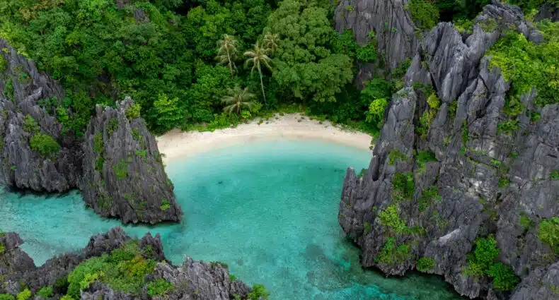 Vista aérea de uma lagoa azul-turquesa cercada por vegetação exuberante e penhascos rochosos. Mostra a Praia Secreta em El Nido, nas Filipinas. Representa o post de melhores praias nas Filipinas.