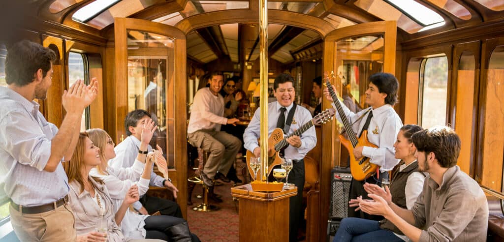vagão observatório com músicos tocando violão e guitarra ao vivo, ao redor de turistas alegres e batendo palma
