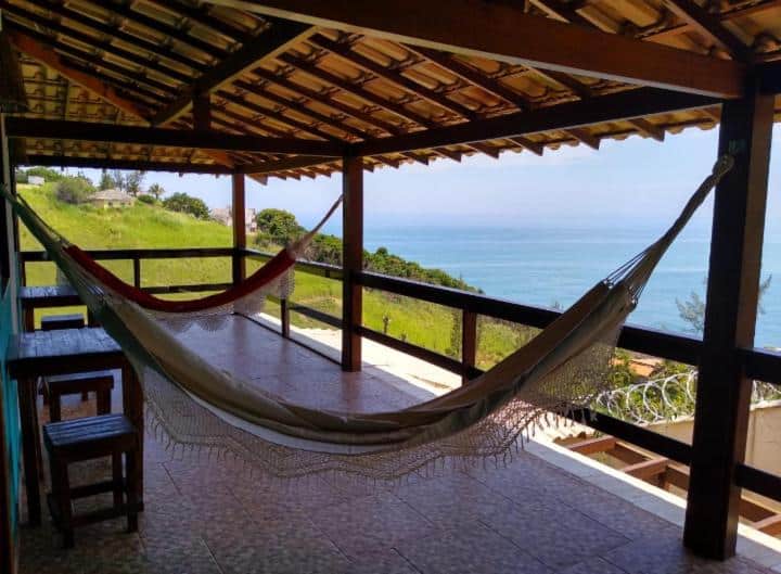 Varanda do Farol House com vista para o mar. A varanda com mesas, bancos e redes de descanso.
