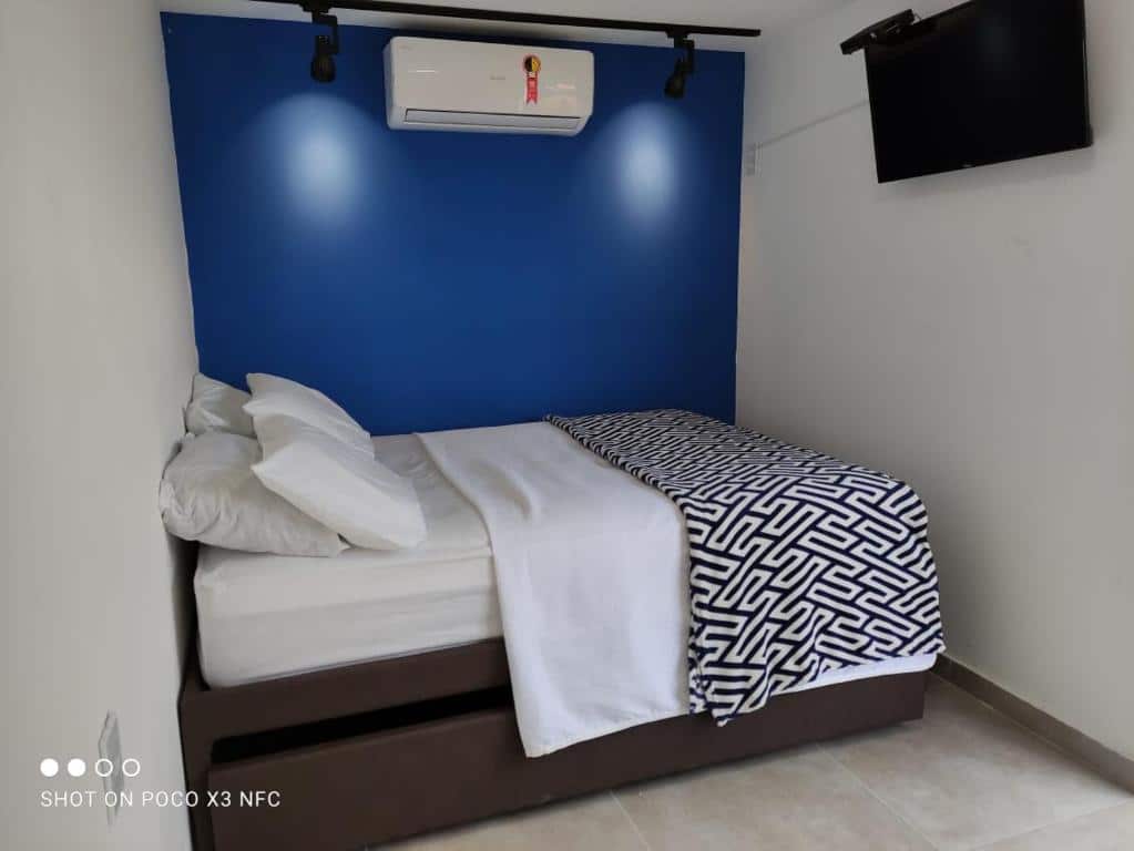 Quarto do airbnb Flat Container Pontal do Atalaia. A cama de casal está encostada no fundo do quarto e em baixo da cama há outro colchão. Na parede em frente a cama há uma TV presa a parede. Imagem utilizada para ilustrar o post airbnb em Arraial do Cabo.