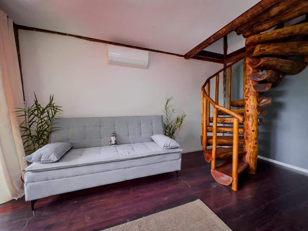 Sala de estar do airbnb Flats Apple Ilha com Banheira. No canto esquerdo está o sofá da sala, na frente há um tapete e no lado direito há uma escada em formato espiral feita de madeira. 