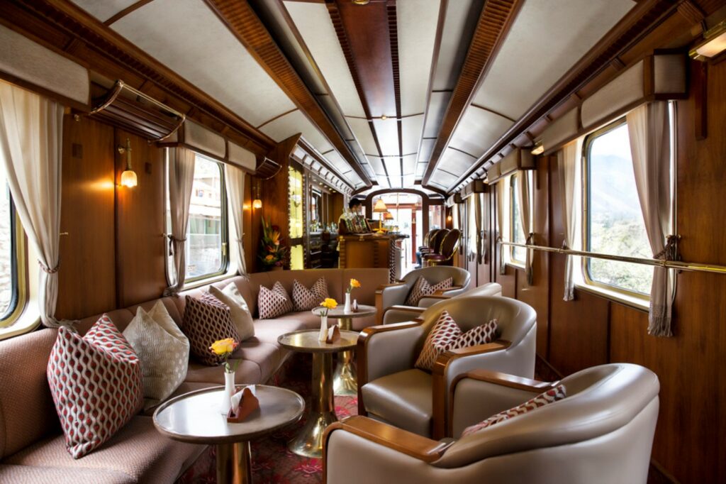 luxuoso vagão do hiram bingham perurail com vários sofás e poltronas, além de um bar ao fundo.