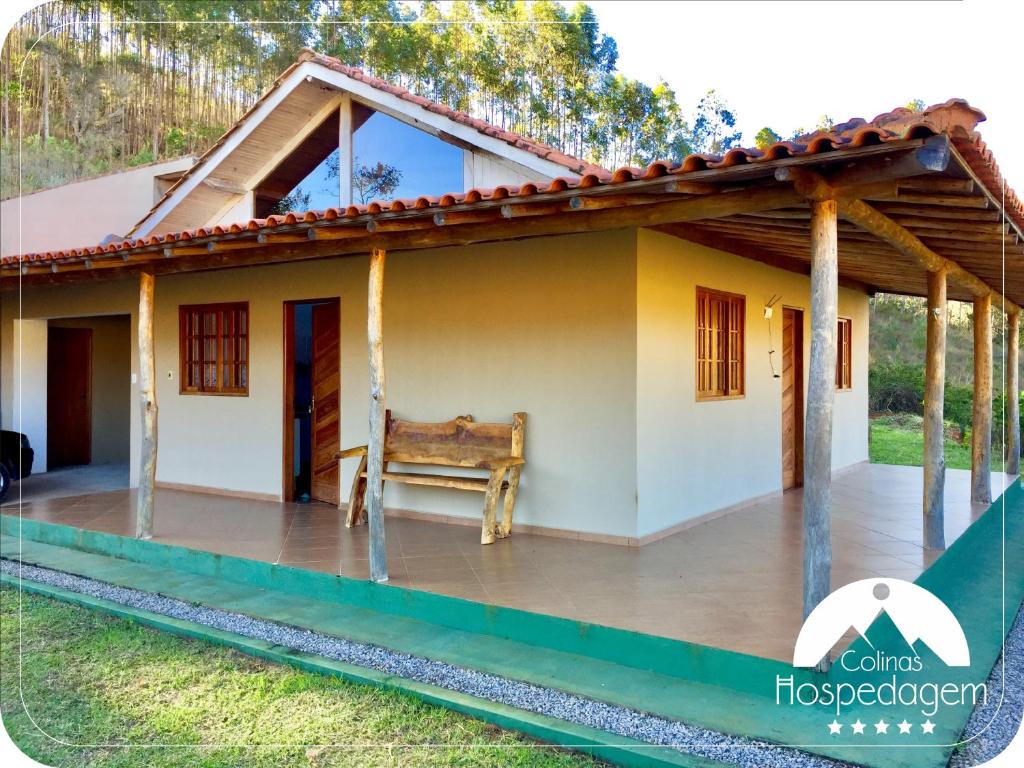 Fachada da Hospedagem Colinas que mostra a construção da casa térrea com duas portas de madeira e três janelas, um banco de madeira e uma garagem para carros. A casa tem telhado de telhas com pilastras e apoio de madeira. Imagem ilustrando post Airbnb em Aiuruoca.